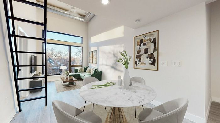 Dining area in Denver apartments featuring large windows, a view of the cozy living room, and stairs leading to a flexible loft space for work or relaxation.