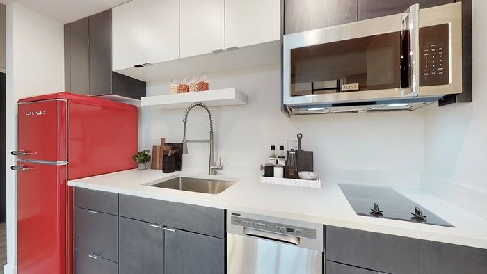Luxury kitchen in Denver apartments with stainless steel appliances, quartz counters, and a modern red refrigerator for a stylish touch.
