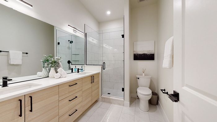 Modern bath with dual sinks, light colored cabinets, white quartz counters, and tiled shower enclosure with glass frameless shower door