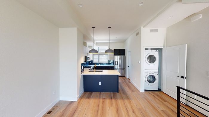 Modern kitchen with colorful tile backsplash, two-tone cabinets, stainless steel appliances, French door refrigerator, wood-style flooring, and pendant