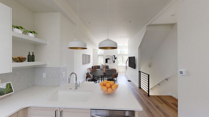 Kitchen peninsula with bar seating overlooking dining area and living room in the distance, featuring wood-style flooring, iron railing on stairs, and large windows
