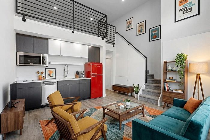 Modern apartment living space with a stylish loft, vibrant red fridge, sleek kitchen, and cozy seating area with colorful decor.
