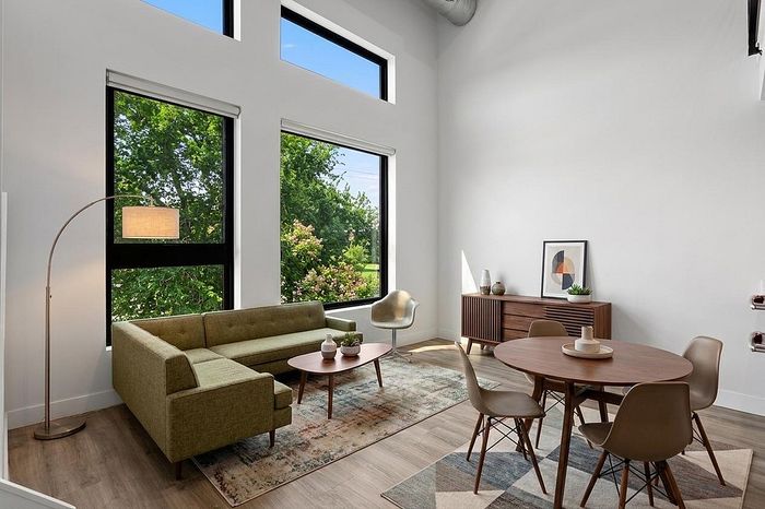 Bright, modern living room with stylish furniture, large windows showcasing greenery, and contemporary decor.