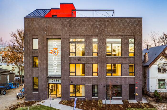 Modern urban apartment building with a stylish brick facade, large windows, and inviting entrance at dusk.