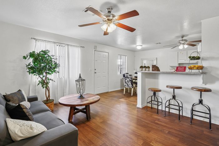 Inviting living area with sleek wood floors, modern ceiling fans, and an elegant open-plan design featuring comfortable seating and a chic breakfast bar.