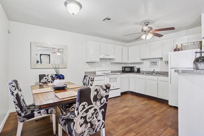 Charming open-concept kitchen and dining area featuring sleek white cabinetry, elegant decor, and a cozy dining table set on rich wooden flooring.