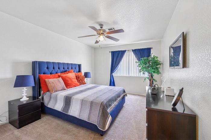 Inviting bedroom with a plush blue headboard, vibrant orange accent pillows, and elegant blue curtains, creating a cozy and stylish ambiance.