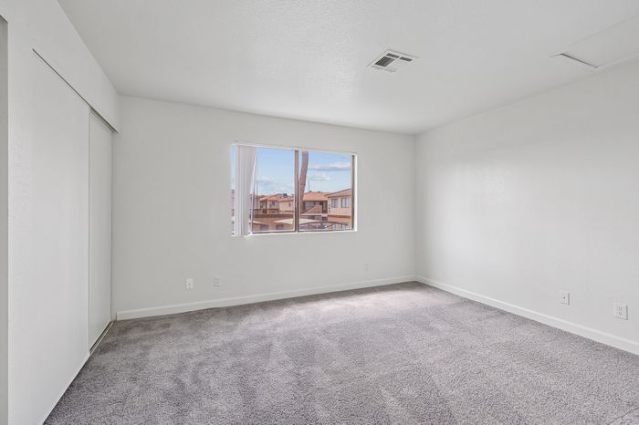 Bright and spacious empty room with plush carpet and large window offering scenic views of neighboring rooftops.