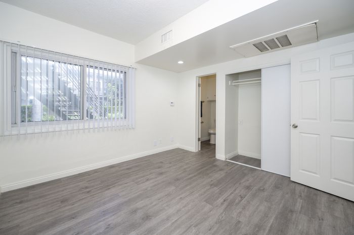 Modern and bright bedroom with sleek laminate flooring, large window with blinds, spacious closet, and an en-suite bathroom.