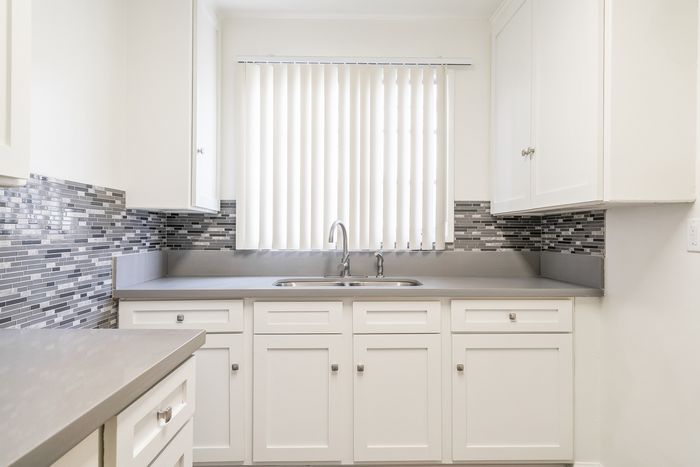 Bright and modern kitchen with sleek gray countertops, elegant white cabinetry, and stylish mosaic tile backsplash.