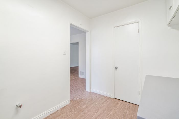 Bright, minimalist hallway with white walls and sleek wooden flooring leading to spacious rooms.