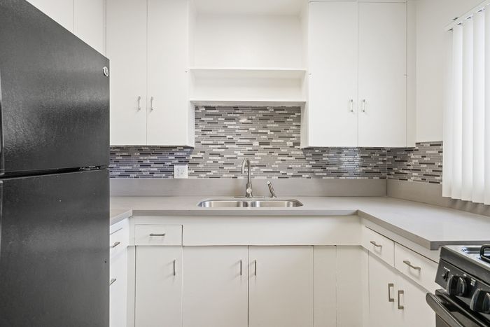 Modern kitchen with sleek black refrigerator, elegant tiled backsplash, and ample white cabinetry.