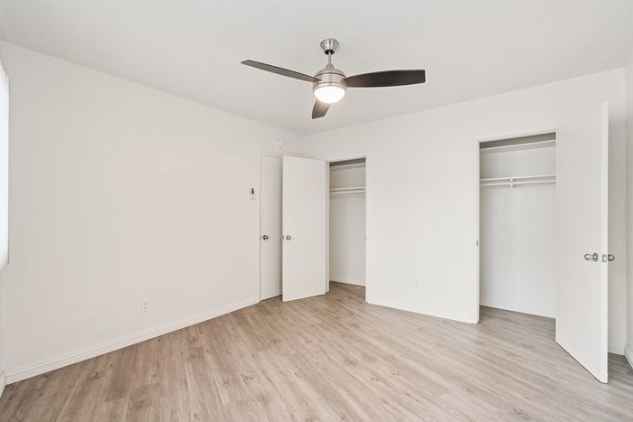 Bright and spacious bedroom with elegant hardwood flooring, sleek ceiling fan, and ample closet space.