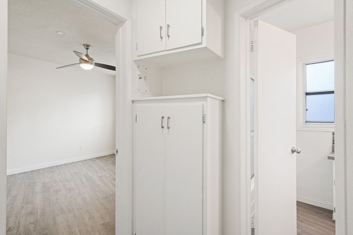 Bright hallway featuring elegant white cabinetry, leading to a room with modern ceiling fan, and adjacent bathroom with natural light.
