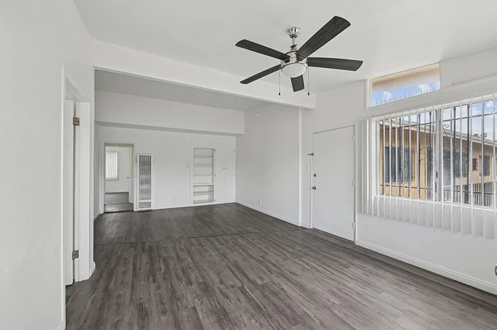 Bright and spacious living room with modern ceiling fan, large windows, and sleek hardwood floors.