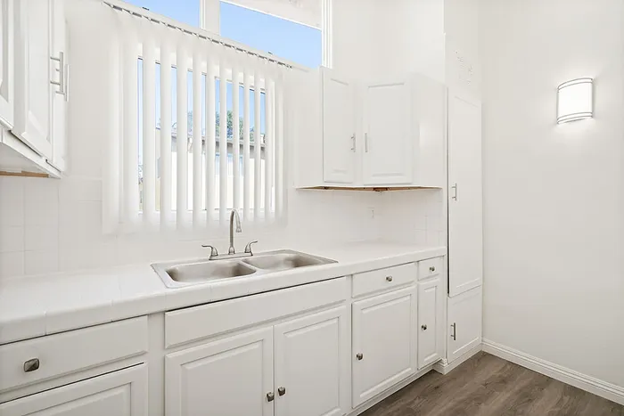 Bright and airy kitchen with elegant white cabinetry, sleek countertops, and modern dual sink framed by natural light from generous windows.