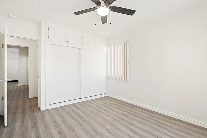 Bright and spacious bedroom with modern ceiling fan, elegant closet space, and sleek hardwood floors.