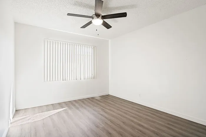 Bright and airy room with sleek wood flooring and a modern ceiling fan, offering an inviting blank canvas for personalization.