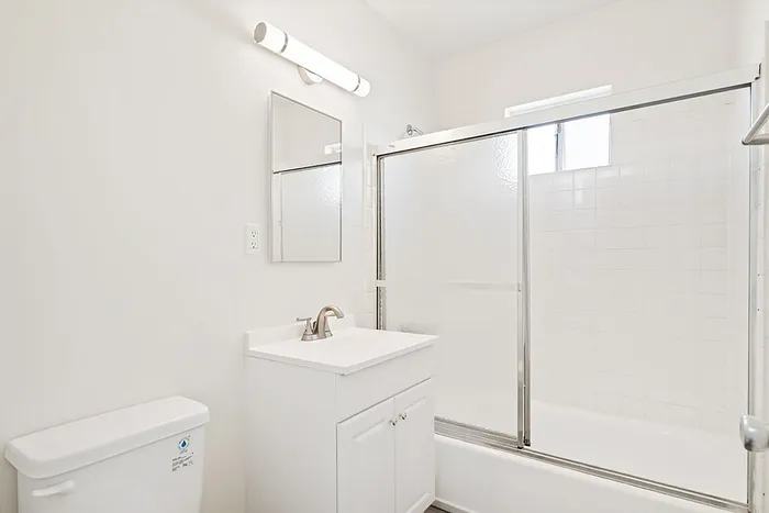 Bright, modern bathroom with sleek white vanity, elegant mirror, and spacious shower with sliding glass doors.