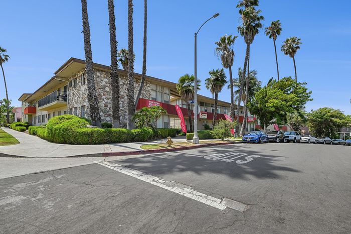 Charming residential building with stone fa&ccedil;ade and lush landscaping, lined with palm trees and situated on a sunny corner.