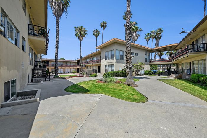 Charming apartment complex featuring lush green lawns, palm trees, and modern architecture, perfect for comfortable living.