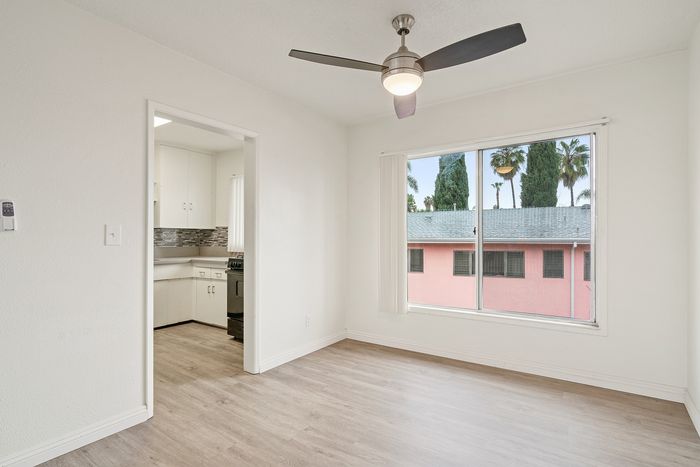 Bright apartment interior with a sleek ceiling fan, large window view of palm trees, and modern kitchen entrance.