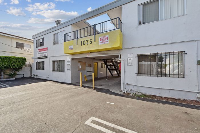 Charming apartment building with a bright yellow awning and secure gated entry, offering convenient parking.