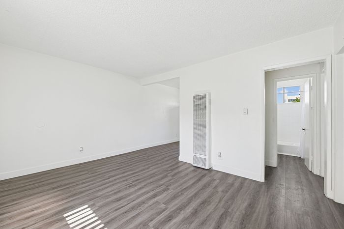 Sleek and spacious living area with elegant wood flooring, ample natural light, and crisp white walls, leading to a bright bathroom.