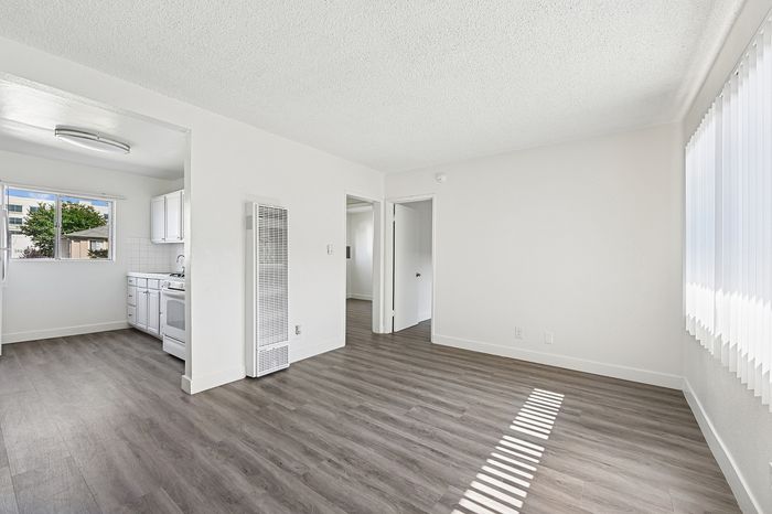 Bright, airy living space with modern laminate flooring, large window for natural light, and adjacent kitchen perfect for comfortable living.