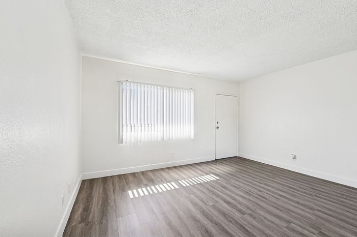 Bright and airy room with modern wood flooring, a large window with vertical blinds, and minimalist white walls, perfect for customizing your dream space.