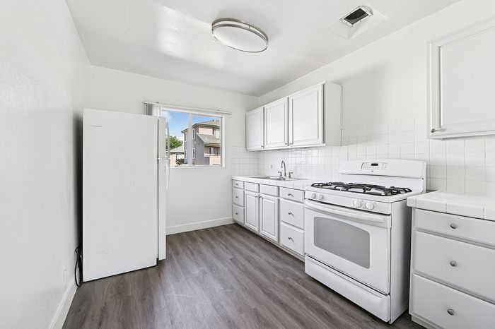 Bright and airy kitchen with modern white cabinetry, sleek flooring, and ample natural light from a picturesque window.