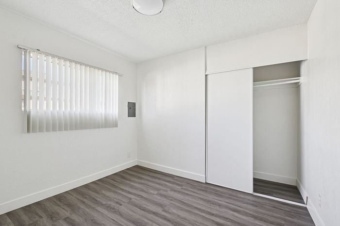 Bright and airy room with sleek flooring, large window with vertical blinds, and a spacious closet, perfect for a modern living space.
