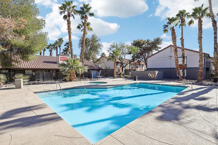 Inviting pool area surrounded by picturesque palm trees and a sunlit patio in a serene apartment complex.