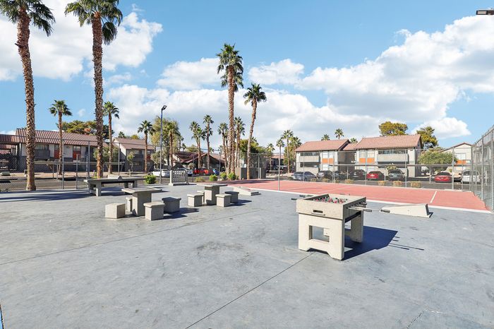 Vibrant outdoor recreation area featuring palm trees, a tennis court, and a foosball table under a clear blue sky.