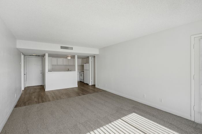 Bright and spacious living area with modern open-plan kitchen, featuring elegant neutral tones and a mix of carpet and wood flooring.
