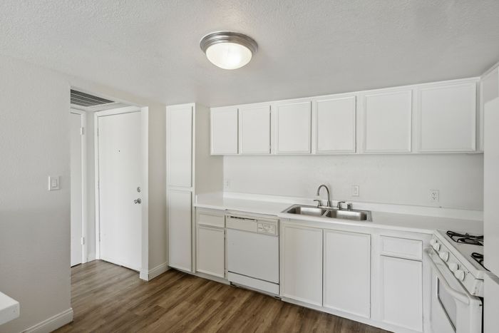 Bright, modern kitchen with sleek white cabinetry, dual sink, and classic wood flooring.