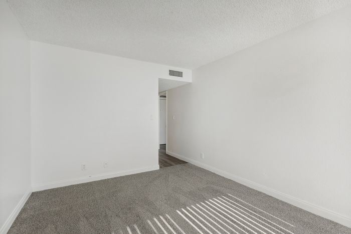 Bright, open corner room with soft carpeting and neutral walls, perfect for personalization and cozy living.