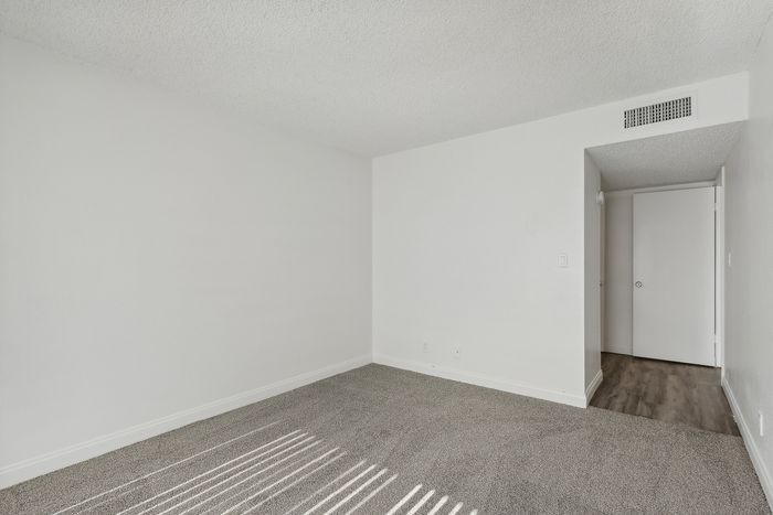 Bright and airy room with a neutral palette, plush carpet, and sleek doorway, perfect for a cozy retreat.