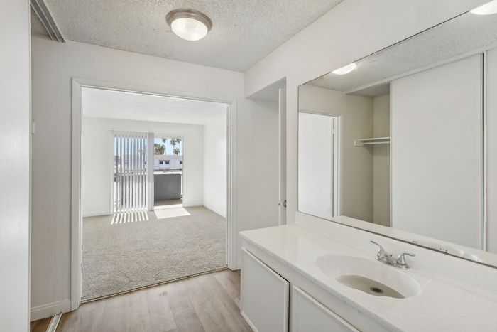 Inviting apartment hallway leading to a bright room with balcony access, featuring elegant hardwood floors and a sleek modern sink.