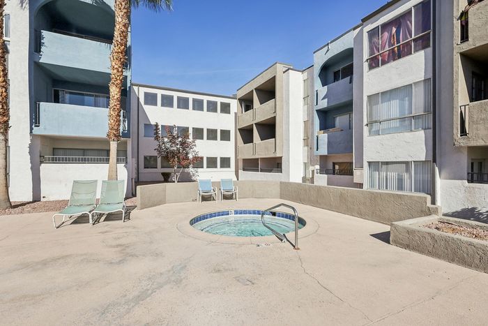 Charming apartment complex with a serene courtyard featuring a bubbling hot tub and comfortable lounge chairs under clear blue skies.