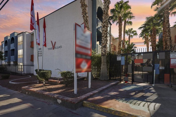 Charming apartment complex, The Villas, with elegant landscaping and a modern gated entrance, set against a beautiful sunset sky.