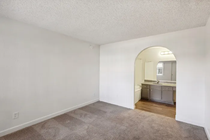 Inviting room with soft carpet flooring leading to a stylish bathroom through an elegant archway, featuring modern vanity and warm lighting.