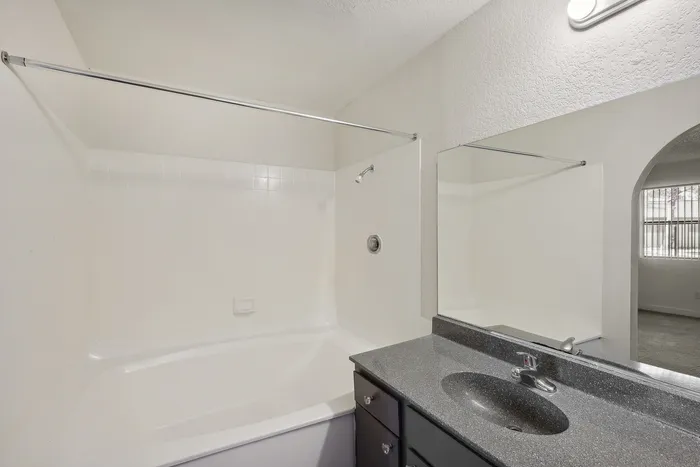 Modern bathroom with sleek granite countertop, large mirror, and pristine bathtub, inviting relaxation and style.