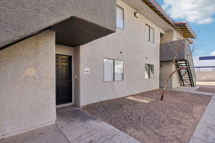 Inviting apartment exterior with modern design, featuring a welcoming entryway and outdoor staircase under a clear blue sky.