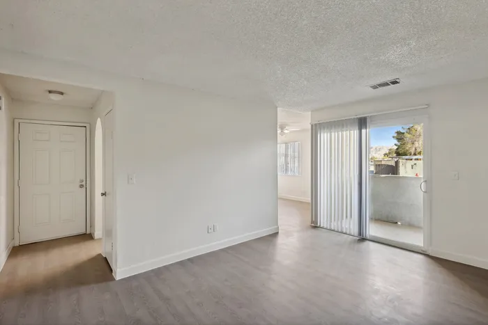 Bright entrance of a modern apartment with sleek flooring and sliding glass doors leading to a sunlit balcony.