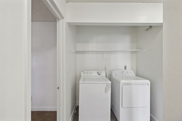 Modern laundry nook featuring a sleek washer and dryer set with a convenient overhead shelf in a bright, white-walled space.