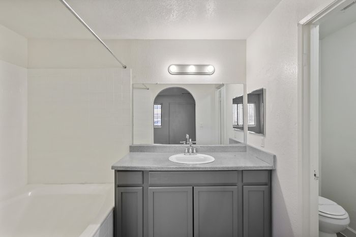 Bright bathroom with sleek vanity, large mirror, and white tiled bathtub, offering modern and clean aesthetics.