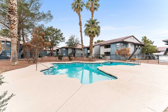 Inviting outdoor pool surrounded by palm trees and modern apartment buildings, offering a serene living experience.