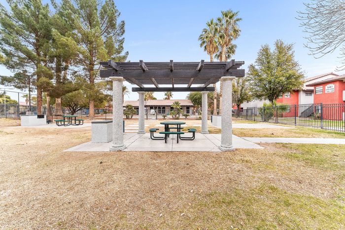 Inviting outdoor space featuring a charming pergola with picnic tables, surrounded by lush greenery and towering palm trees in a tranquil community setting.