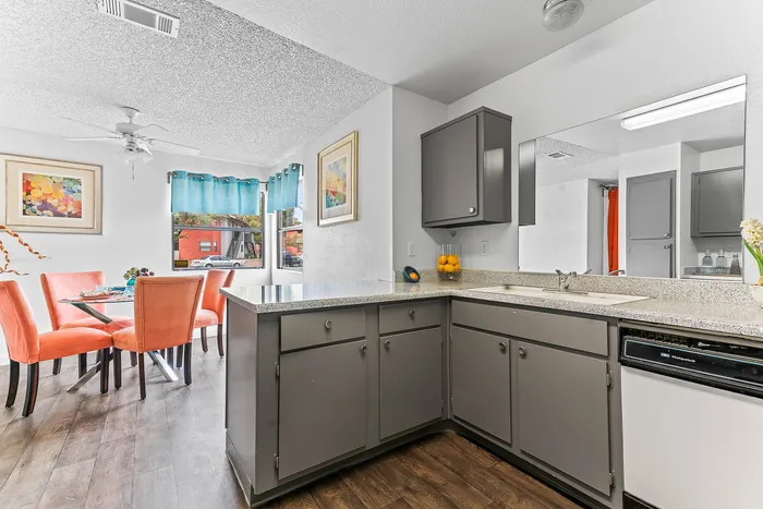 Bright kitchen and dining area with modern gray cabinets, vibrant coral chairs, and artistic decor, creating a welcoming and stylish atmosphere.